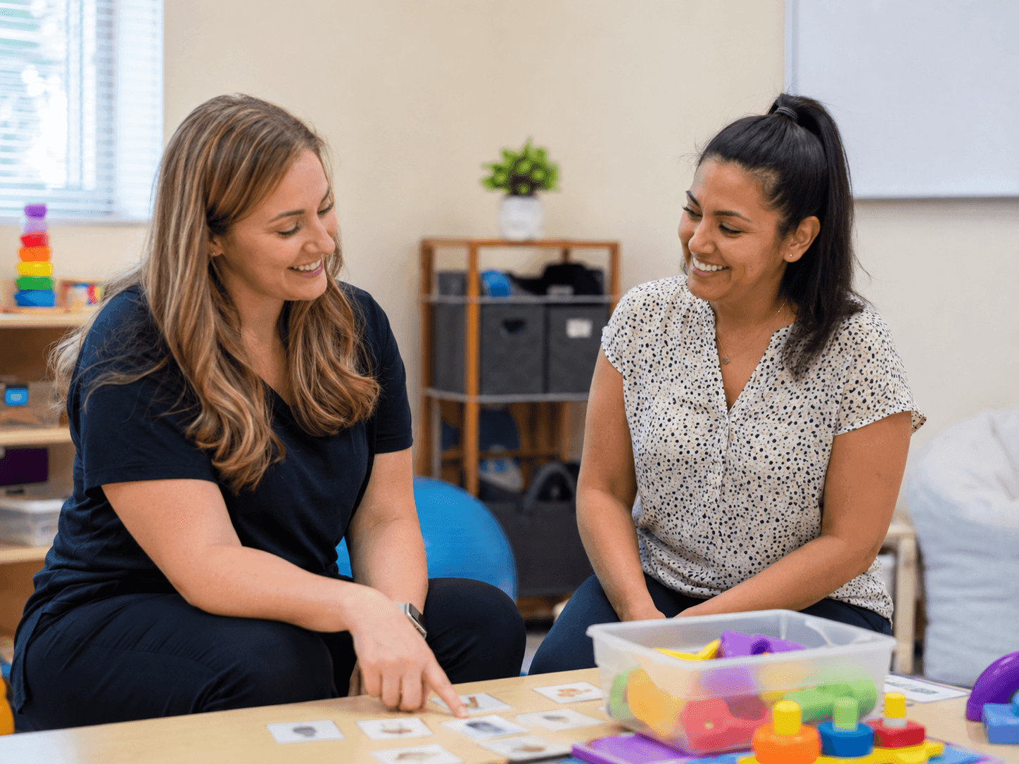 Two Enlight clinicians collaborating over picture cards and toys in a therapy room
