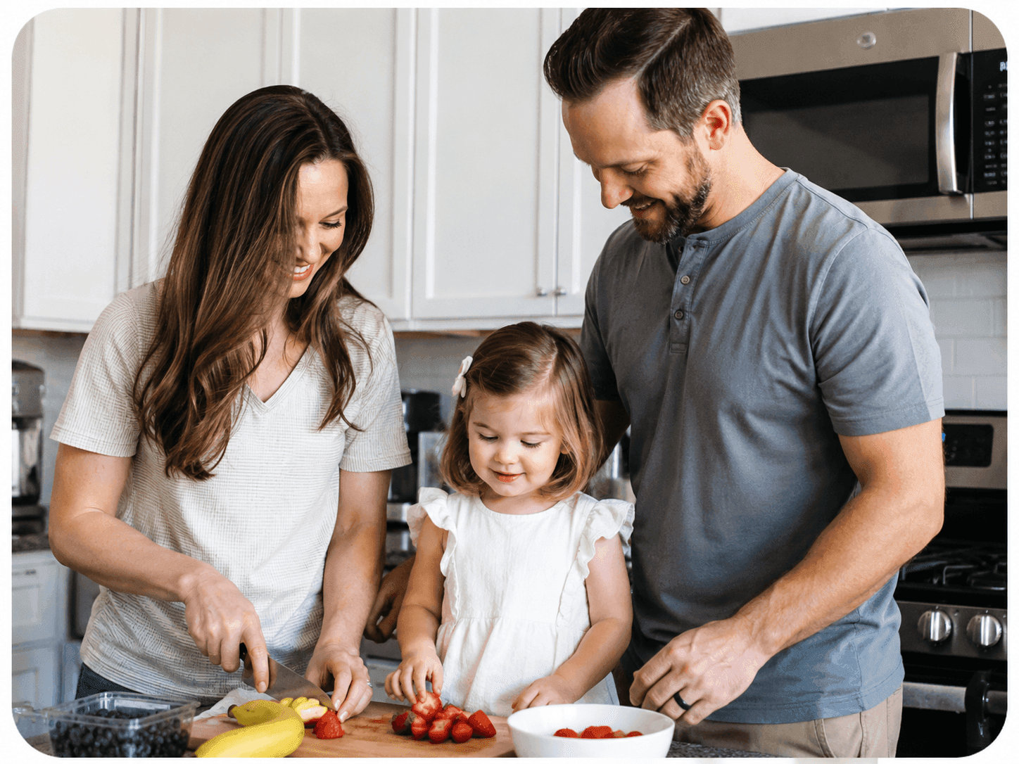 A mother, father, and young daughter slicing fruit together in the kitchen