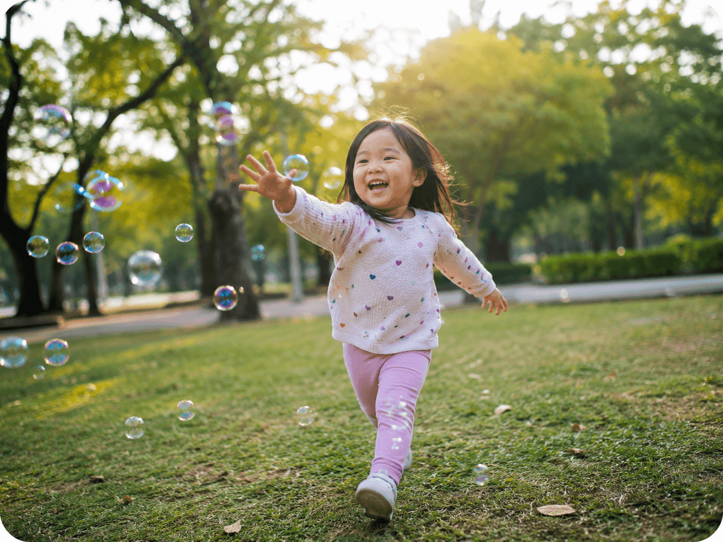 A laughing toddler reaching for bubbles in a sunlit park